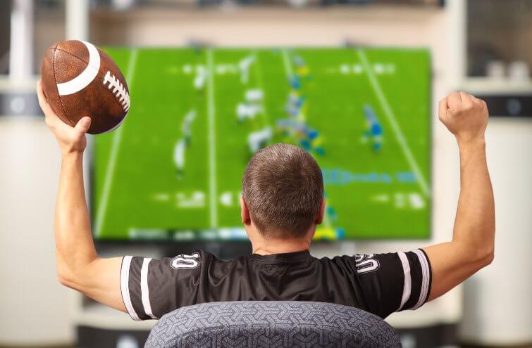 Fan of american football. Man with a ball watching TV.